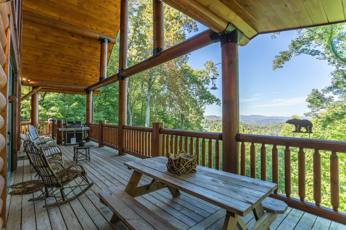 A tranquil porch with rocking chairs and a picnic table overlooking panoramic mountain views. The decorative animal sculpture adds a playful, pet-friendly touch, while the open space around the porch hints at pet accessibility and mountain exploration.