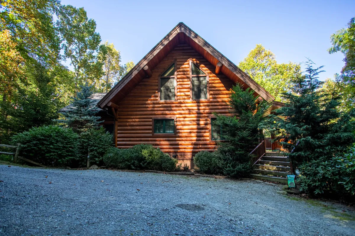 A welcoming view of the log cabin's facade, complete with a landscaped garden and stone steps leading to the entrance. The inviting atmosphere is perfect for families arriving at the lodge, surrounded by lush greenery that hints at the adventure awaiting in the mountains.