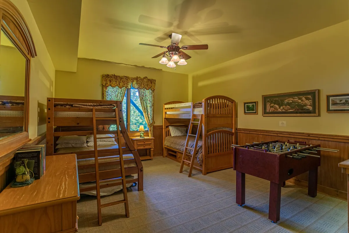 A playful interior featuring multiple bunk beds and a foosball table, with natural light streaming in through the window. The space is clearly designed for group fun and late-night gatherings, echoing the description of a dedicated bunk room for kids or friends.