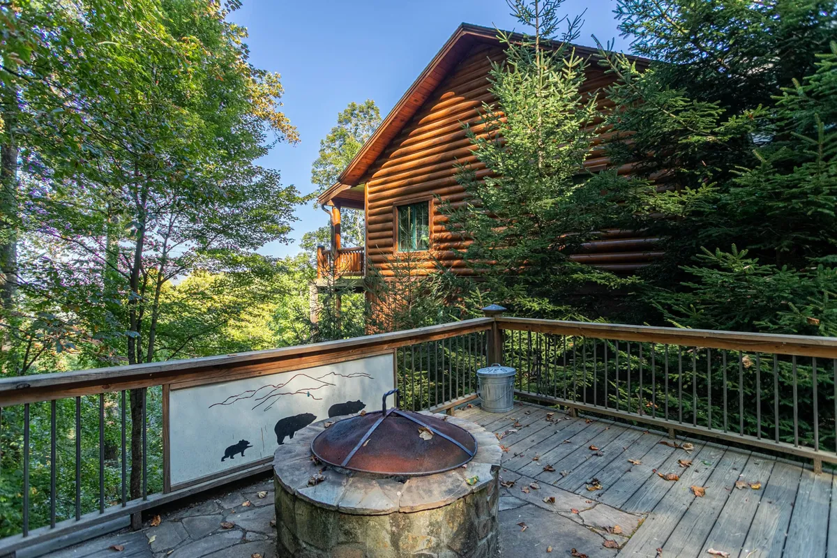 A spacious wooden deck nestled among the trees, featuring a cozy fire pit surrounded by seating. The area radiates the promise of outdoor gatherings, stargazing, and storytelling after a day of exploring the local area.
