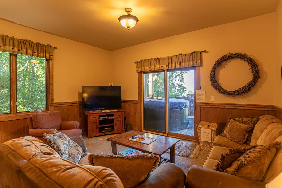 A comfortable media lounge with plush sofa seating faces a large television, with a coffee table and expansive windows allowing natural light to fill the room. A wreath adds a touch of warmth to the decor.
