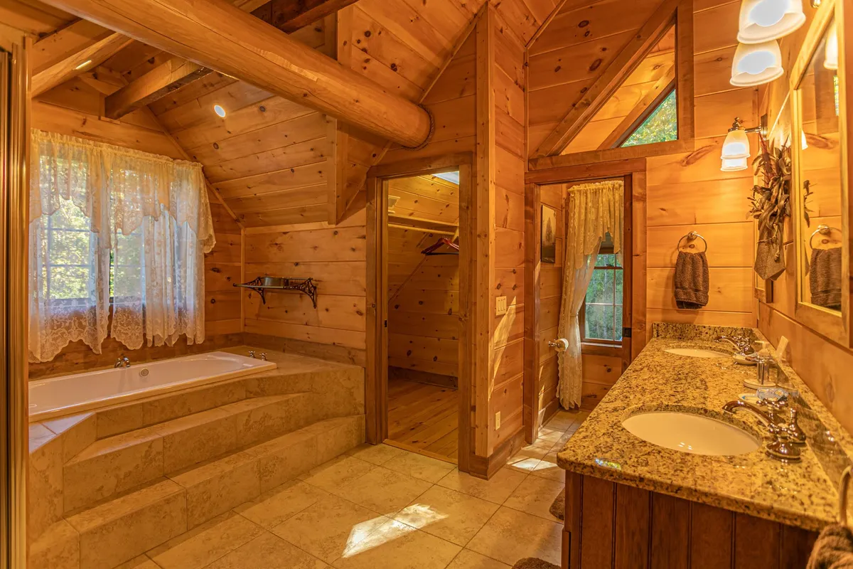 A bathroom with a luxurious soaking tub, dual sinks set in a granite countertop, wooden accents, and large windows that let in plenty of natural light. The space feels tranquil and spa-inspired.