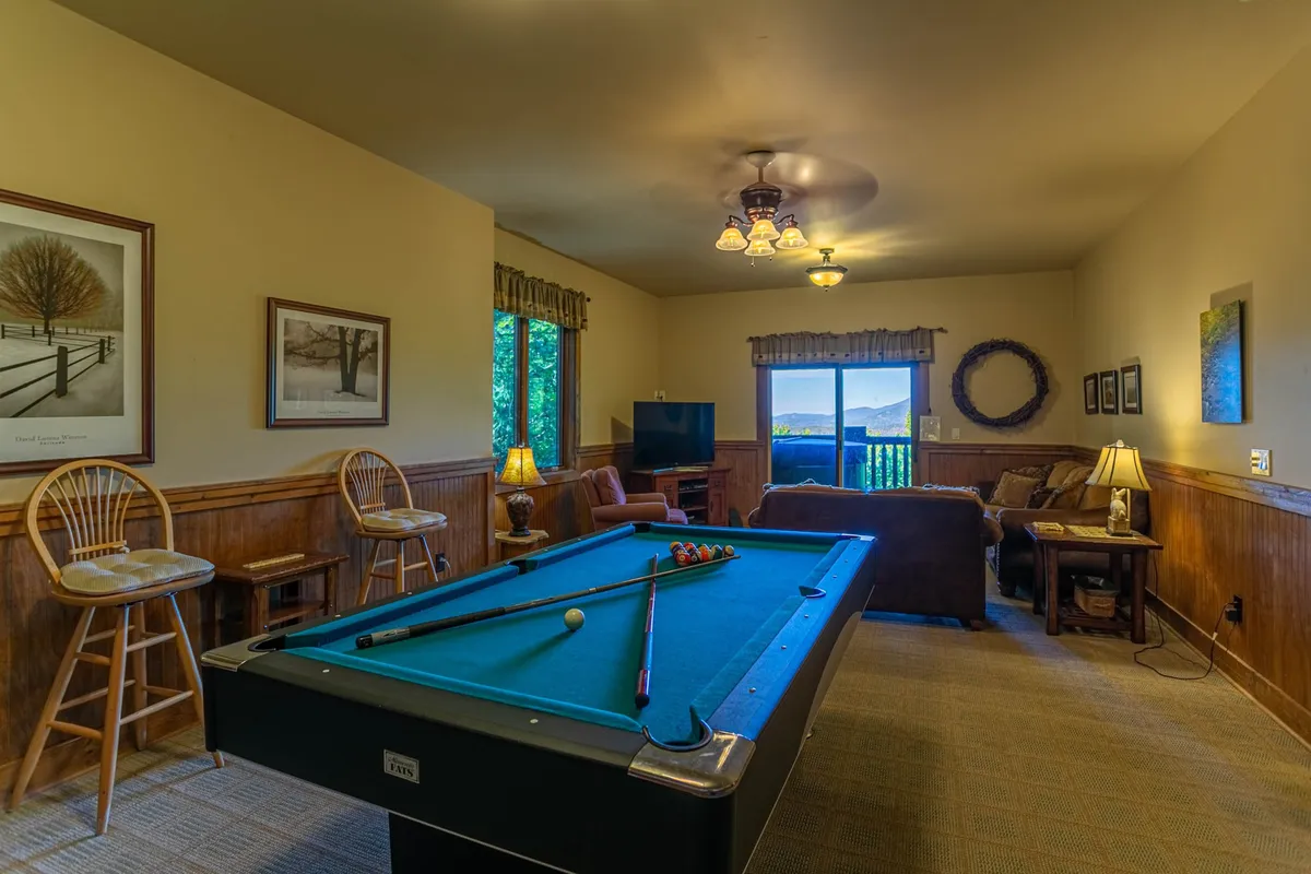 This image captures a vibrant recreation room featuring a pool table, comfortable sofa seating, a window with scenic views, and framed artwork on the walls. The space is well-lit and invites both casual relaxation and lively gameplay.