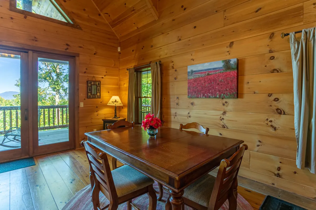 A wooden dining table adorned with a vase of flowers sits beside expansive glass doors, offering a glimpse of the outdoors. The space feels connected to nature while remaining warm and inviting, ideal for shared meals or enjoying mountain sunsets.