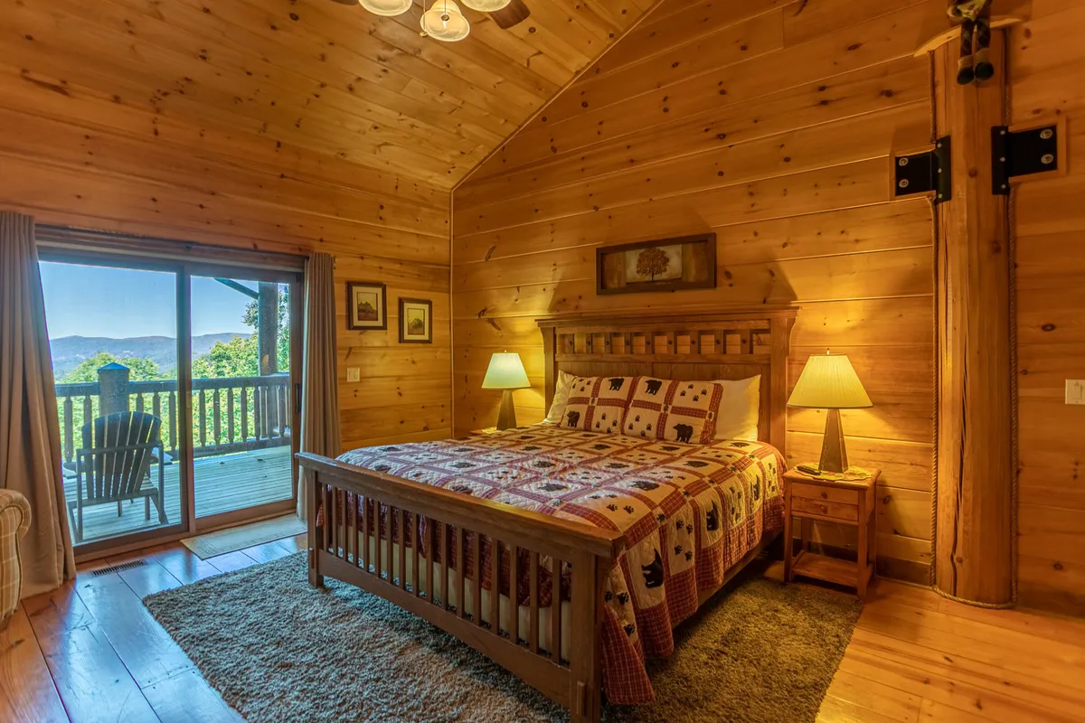 This image features a wooden bed frame with a colorful quilt, a nightstand with a lamp, and a sliding glass door that opens out to nature. The room is bright and inviting, offering a sense of privacy and direct access to the outdoors, which is ideal for representing the master king suite described in the section.