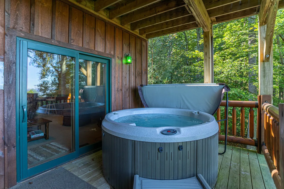 A serene outdoor hot tub set on a wooden deck, surrounded by greenery and adjacent to a sliding glass door. The space hints at evenings spent in conversation beneath the stars or relaxing after a day of local exploration, perfectly complementing the idea of group storytelling by the fire or winding down after a hike.