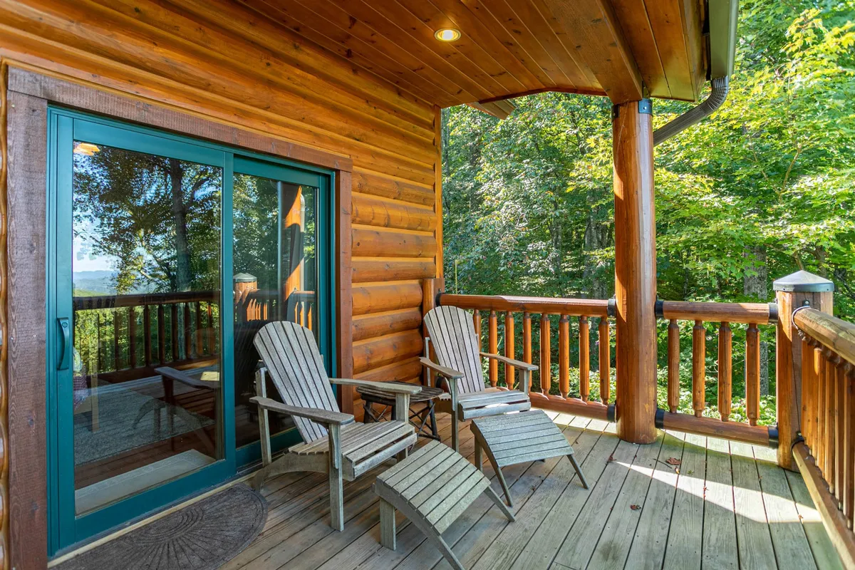 A tranquil wooden deck featuring several rocking chairs set against a backdrop of lush trees. Sliding glass doors connect the deck to the interior, illustrating easy flow between inside and outside spaces—ideal for group members to mingle or find moments of quiet reflection while still close to the action.